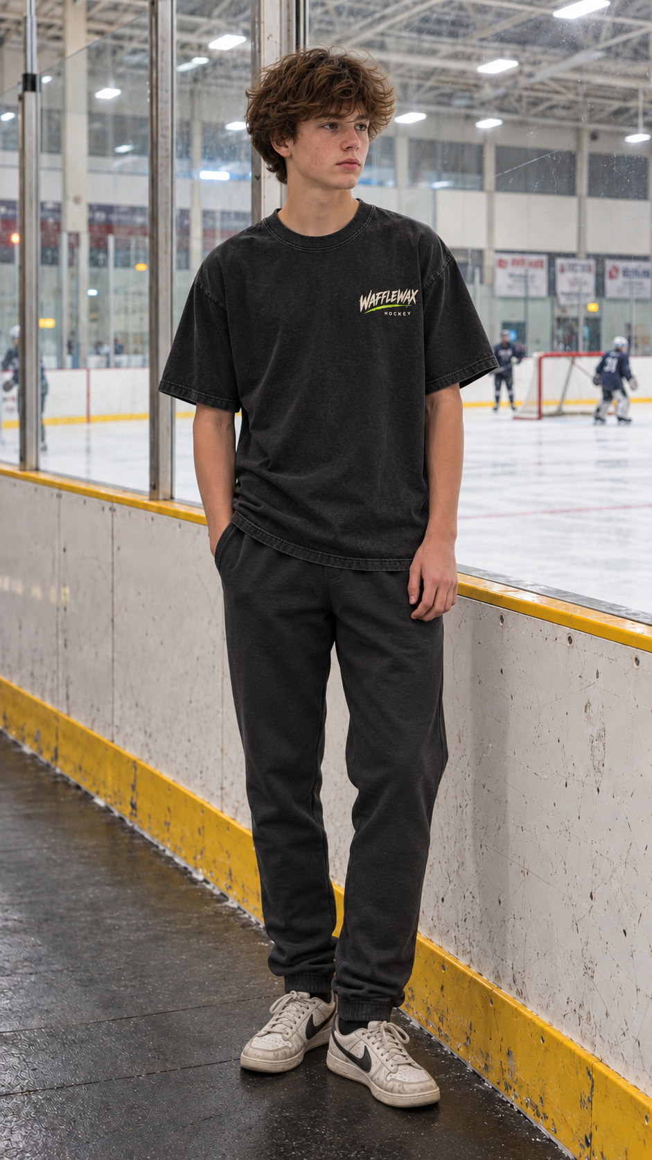 Front view of the washed-black WaffleWax Stay Saucy tee with a small cream and lime left-chest logo, worn at an ice rink.